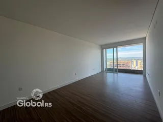 Ambiente interno de uma sala com piso de madeira e vista para a cidade.