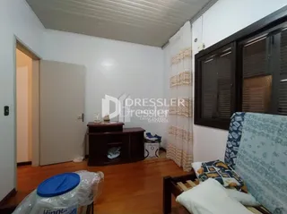 Quarto com piso de madeira e cabeceira de cama visível.