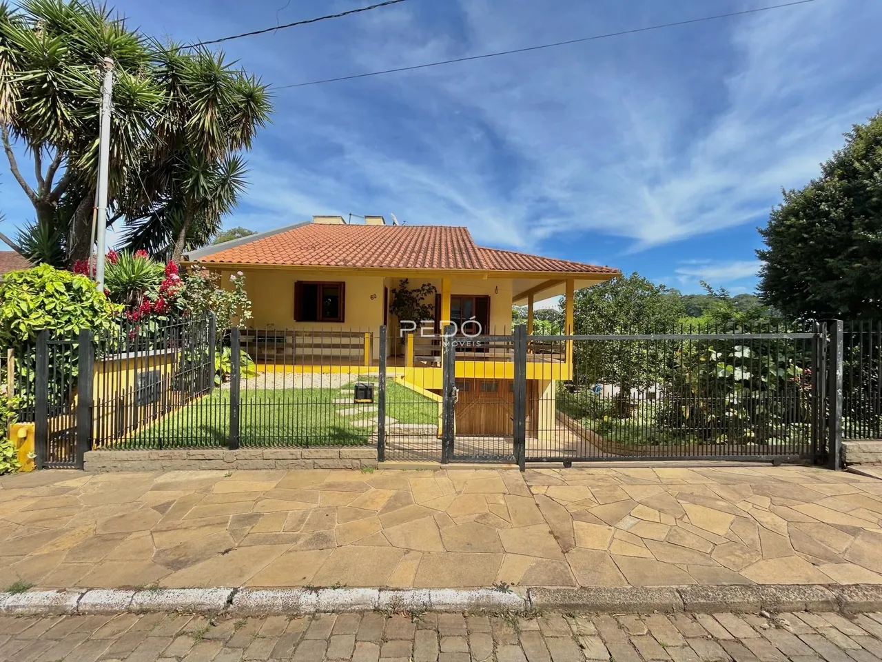 Fachada de uma casa amarela em Lajeado, Brasil, com cerca e portão de ferro.