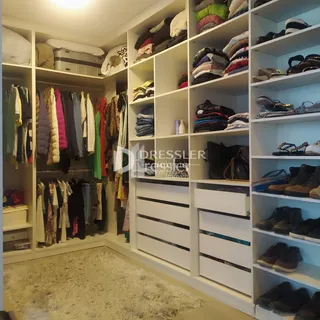 Armário branco com prateleiras cheias de roupas em um ambiente interno.