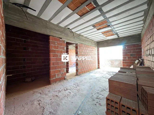Interior de uma estrutura em construção com paredes de tijolo aparente e piso cru.