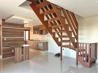 Interior de uma sala de estar com cozinha e escadaria em um imóvel no Brasil.