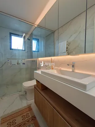 Banheiro moderno com revestimento em mármore e bancada branca.