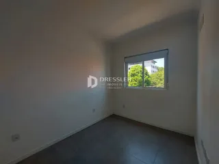 Parede branca de uma sala com uma janela que oferece uma vista externa.