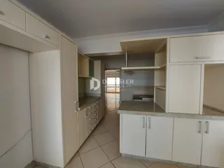 Vista interna de uma cozinha com armários brancos e piso de cerâmica.