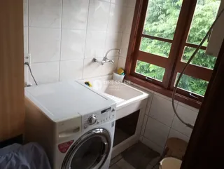 Imagem de um banheiro com máquina de lavar roupa e janela com vista para a natureza.