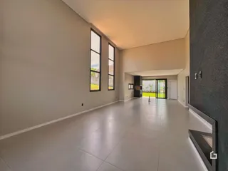 Ambiente interno de uma sala ampla com piso claro e grandes janelas.