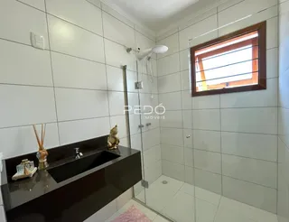 Interior de um banheiro com revestimento branco e box de vidro.