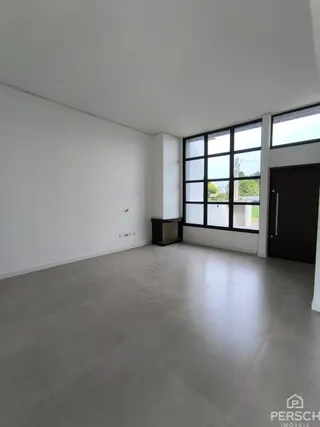 Ambiente interno amplo com paredes brancas e grandes janelas.