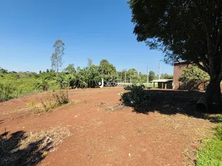 Vista externa de um terreno com vegetação e uma estrutura de tijolos sob um céu azul.