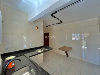 Vista de uma área de cozinha com revestimento de azulejos brancos e bancada escura.