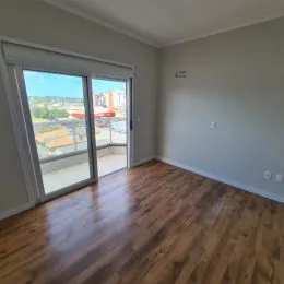 Foto interna de um cômodo com piso de madeira e uma grande janela com vista.