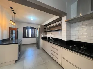 Cozinha moderna com armários brancos e bancadas escuras em um imóvel no Brasil.