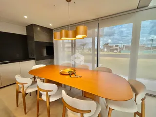 Uma mesa de jantar de madeira com cadeiras brancas é vista em um ambiente interno.