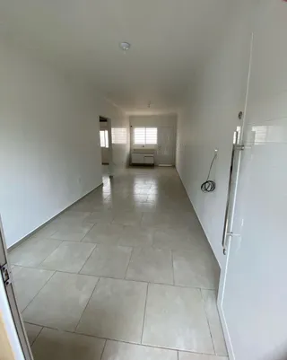 Corredor longo com piso de cerâmica e paredes brancas.