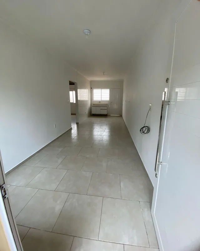 Corredor longo com piso de cerâmica e paredes brancas.