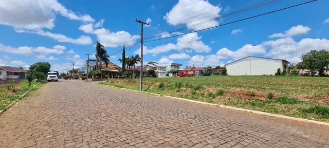Vista externa de uma rua pavimentada com grama e céu azul ao fundo.