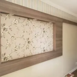 Parede decorada com papel de parede floral e acabamento em madeira clara.