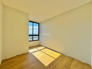 Ambiente interno com piso de madeira e grande janela de vista para a paisagem.