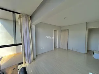 Sala de estar com piso de madeira clara e grandes janelas.