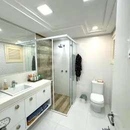 Foto de um banheiro com box de vidro e bancada clara.