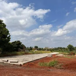 Vista de uma área externa com terra vermelha e vegetação sob um céu parcialmente nublado.