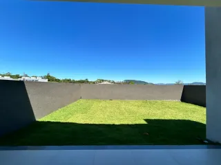 Vista externa de um gramado verde com uma parede de contenção sob um céu azul.