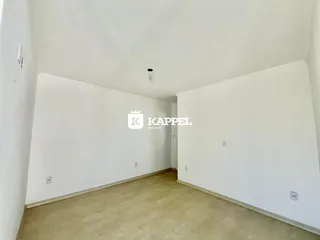 Foto de um cômodo longo e vazio com piso de madeira clara e paredes brancas.