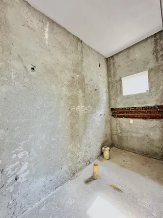Ambiente interno de uma sala com paredes de concreto cru e acabamento em obra.