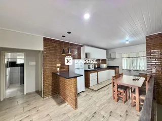 Cozinha com bancada de tijolos aparentes e mesa de jantar em ambiente claro.