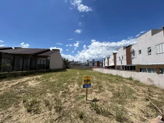 Vista externa de um terreno com grama seca e edifícios residenciais ao fundo.