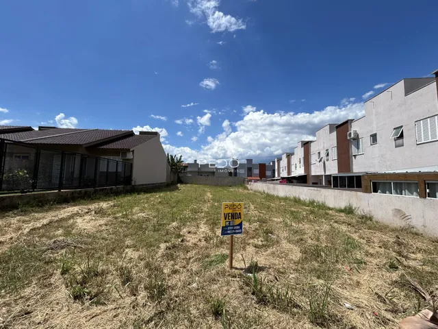 Vista externa de um terreno com grama seca e edifícios residenciais ao fundo.