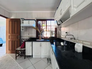 Vista da cozinha com armários brancos e bancadas escuras.