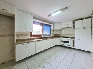 Vista interna de uma cozinha com armários brancos e piso de cerâmica.