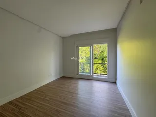Sala de estar com piso de madeira clara e janela de vista para a natureza.