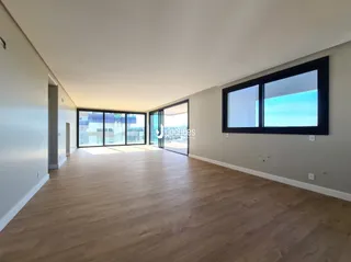 Vista interna de um ambiente com piso de madeira clara e grandes janelas.