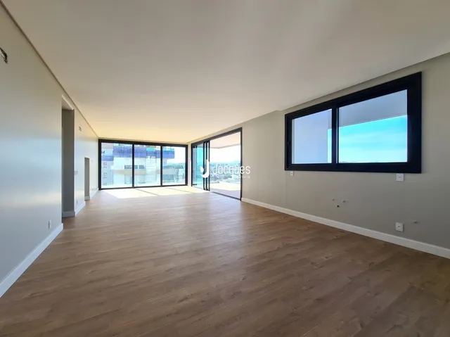 Vista interna de um ambiente com piso de madeira clara e grandes janelas.