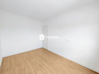 Ambiente interno vazio com piso de madeira clara e paredes brancas.
