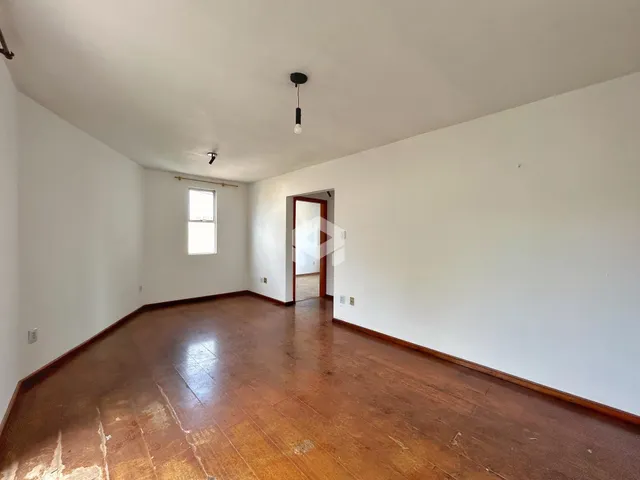Ambiente interno de uma sala com piso de madeira e paredes brancas.