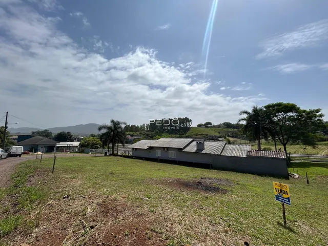 Vista externa de uma propriedade rural com gramado e um imóvel simples.