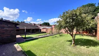 Jardim com gramado verde e árvores ao fundo.