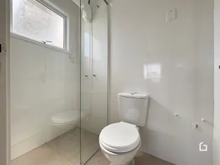 Foto interna de um banheiro com piso cerâmico e box de vidro.