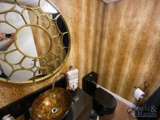 Foto de um banheiro com revestimento dourado e espelho decorativo.