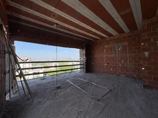 Vista interna de uma área em construção com paredes de tijolo aparente e piso de concreto.