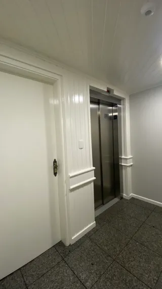 Hall de entrada com painéis brancos e porta de madeira.