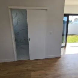 Vista de um interior com porta branca e piso de madeira.