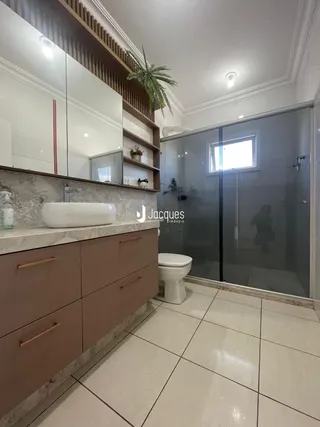 Banheiro com bancada de mármore e box de vidro transparente.