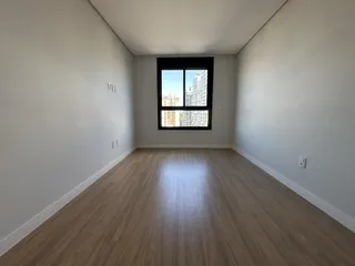 Ambiente interno de uma sala com piso de madeira e janela para a cidade.
