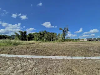 Vista externa de uma área de terreno seca com vegetação no fundo sob um céu azul.