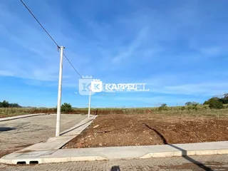 Vista externa de um terreno com asfalto e área de terra seca sob um céu azul.